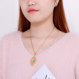 Close-up of gold evil eye jewelry set featuring blue accents on a model wearing pink