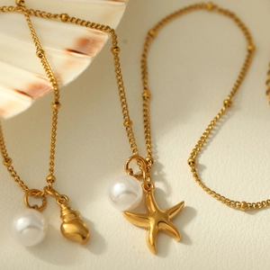 Detail of gold-plated shell and starfish necklaces with pearls on a textured background