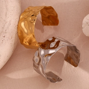 Detailed view of gold and silver hammered metal open cuffs on a textured stone base