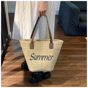 Close-up of beige woven straw tote bag with brown leather handles and Summer embroidery