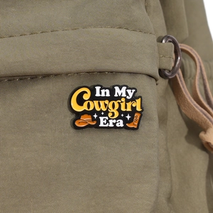 Detail of In My Cowgirl Era enamel pin with cowboy hat on a green canvas bag