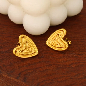 Detail of 18K gold heart stud earrings with layered textures on a dark wood background