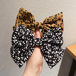 Handheld view of two elegant leopard print bow hair clips in brown and black fabric colors