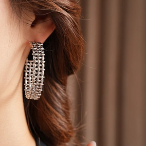 Close-up of silver-tone woven hollow C-shaped hoop earrings worn by a model