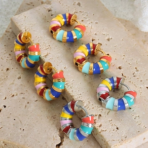Colorful striped enamel hoop earrings with ribbed texture on travertine stone surface