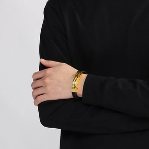 Dettaglio di un bracciale in pelle intrecciata nera con chiusura dorata al polso