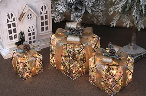Three glowing Christmas gift boxes with gold bows and pine needles for holiday decor