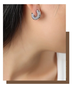 Macro shot of silver C-shaped titanium earrings with paved cubic zirconia on a model