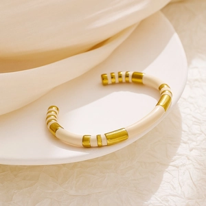 Detailed shot of cream and gold striped enamel bangle on a white ceramic plate