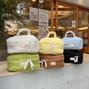 Stack of six colorful teddy plush makeup bags with top handles in a sunny outdoor setting