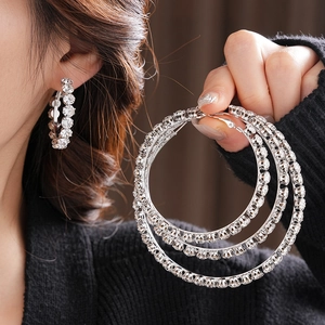 Detail of silver round hoop earrings with clear stones worn by model and held in hand