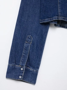 Détail de poignets de veste en jean bleu foncé avec boutons-pression et surpiqûres fines