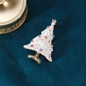 Close-up of white enamel Christmas tree brooch with colorful gemstones on blue velvet