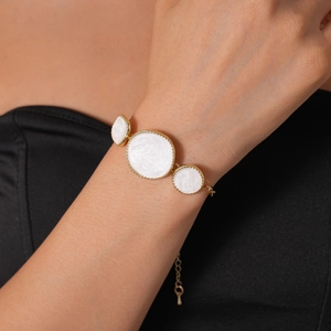 Gros plan d'un bracelet doré ajustable avec trois breloques rondes en émail blanc