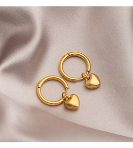 Close-up of gold heart drop earrings on light gray silk background for a luxury look