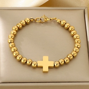 Detailed top view of a gold beaded cross bracelet on a luxurious silk jewelry box cushion