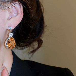 Detail of silver drop earrings with orange zircon stones worn by a model in warm light