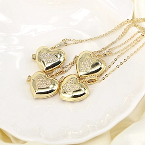 Top view of gold heart lockets with cubic zirconia patterns on white ceramic tray