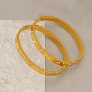 Close-up of gold titanium bangles with floral pavé diamonds and geometric carvings