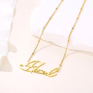 Collier doré avec pendentif Blessed et chaîne satellite sur une pierre texturée blanche