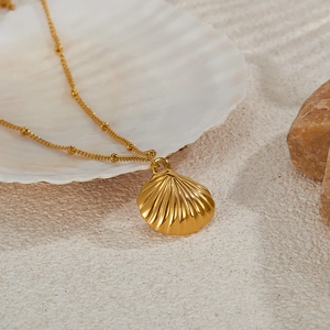 Macro shot of gold shell pendant with bead chain on white shell and sand background