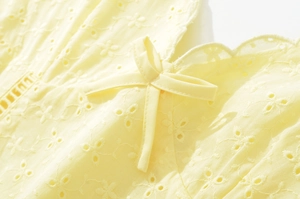 Dettaglio ravvicinato di tessuto ricamato traforato giallo tenue con fiocco