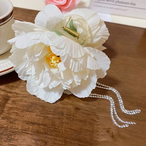 Close-up of white fabric camellia hair claw clip with hanging rhinestone tassels and crystal chains