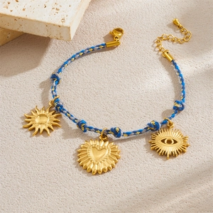 Détail du bracelet tressé bleu et gris avec breloques dorées en forme de soleil, cœur et œil