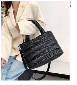 Detail of a black quilted tote bag featuring glossy fabric and adjustable strap