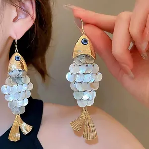 Fish-shaped gold drop earrings with shell inlay and blue eye detail on model