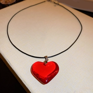 Détail d'un pendentif cœur en résine rouge sur un collier en cordon noir fin