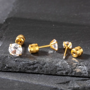 Macro shot of gold stainless steel stud earrings with clear zircon on black rock surface