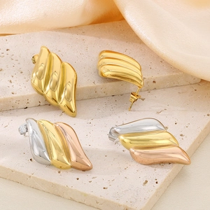 Detail of 18K gold and tricolor plated ribbed wing earrings on elegant stone and silk