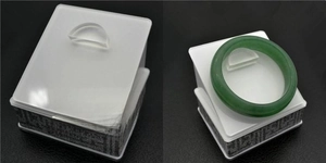 Detail view of a dark green jade bangle atop a white matte display box with Greek fret patterns