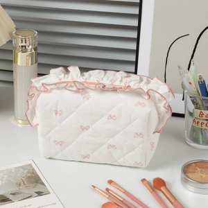 Quilted cosmetic bag with pink bow pattern and ruffled edge detail for makeup tools