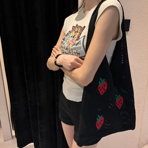Detail of hand-knitted black tote bag with red strawberry embroidery on shoulder strap