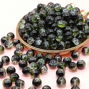 Close-up of 10mm black and green cracked glass beads for DIY jewelry making in a brass bowl