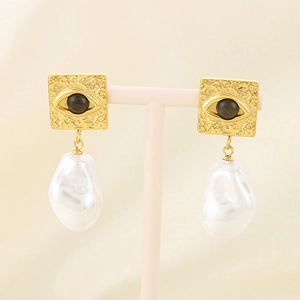 Detailed macro view of gold evil eye earrings with irregular baroque pearl pendants