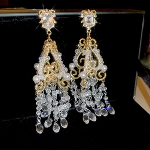 Detailed view of luxury gold tassel earrings with crystals and pearls on black velvet