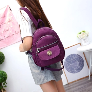 Minimalist purple nylon travel backpack with multi-zipper compartments worn by a model