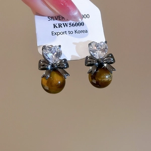 Detail of silver pin earrings with heart zircon, black bow, and brown tiger eye bead