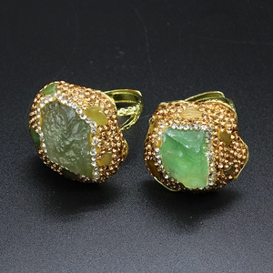 Macro shot of gold ring with raw green gemstone surrounded by sparkling crystals