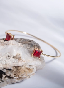 Detail of gold open bracelet with two square red zircon stones on white natural stone