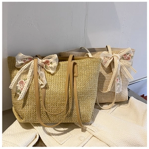 Detail of woven straw tote bag featuring white lace floral bow and leather shoulder straps