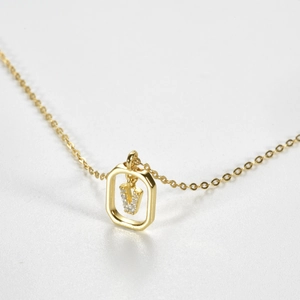 Detail view of a gold hexagonal pendant featuring a sparkling crystal-studded V initial charm