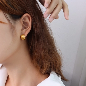 Minimalist C-shaped titanium steel earrings with matte 18K gold finish on a female model