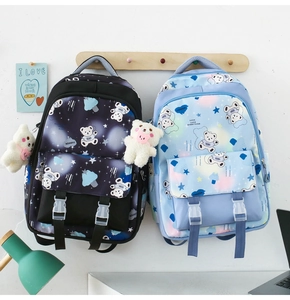 Detail of school backpacks with cartoon bear prints and plush pendants hanging on a rack