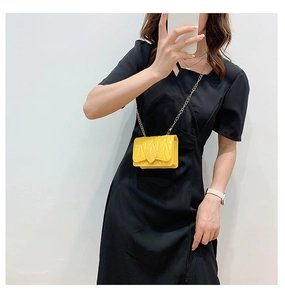Detail of yellow quilted mini crossbody bag with heart clasp and gold chain on model