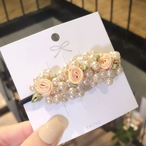 Detail of pearl hair tie with pink silk roses and green leaves on display card