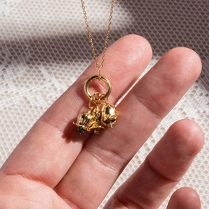 Gold lily of the valley necklace with green stones held against textured fabric
